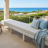 Outdoor bench with white cushion and a blanket on a balcony with ocean view