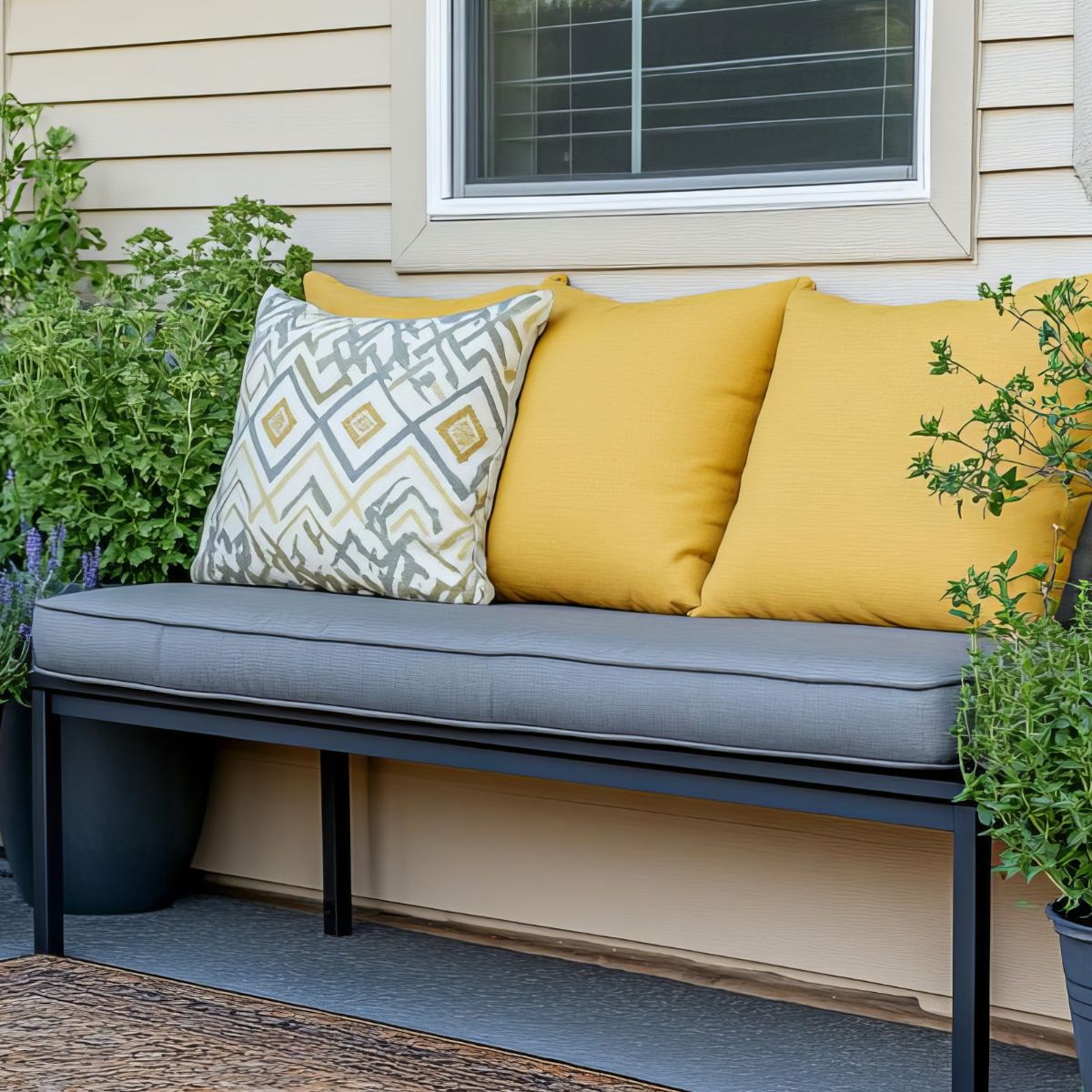 Grey outdoor bench cushion with yellow and patterned pillows